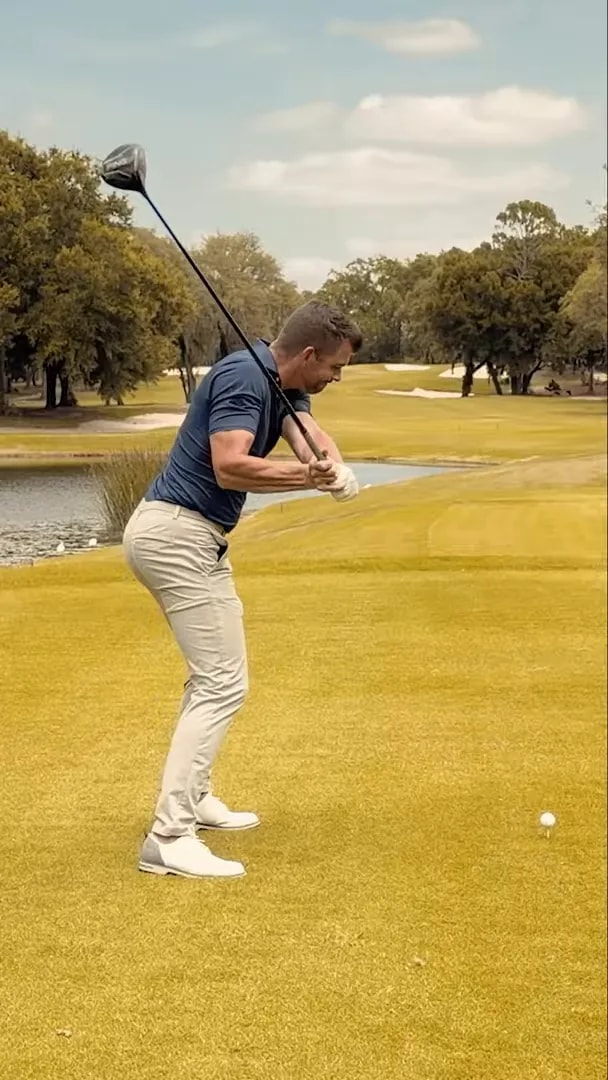 Golfer in downswing with trail elbow working in front of body and driver shaft angled steeply toward the ball