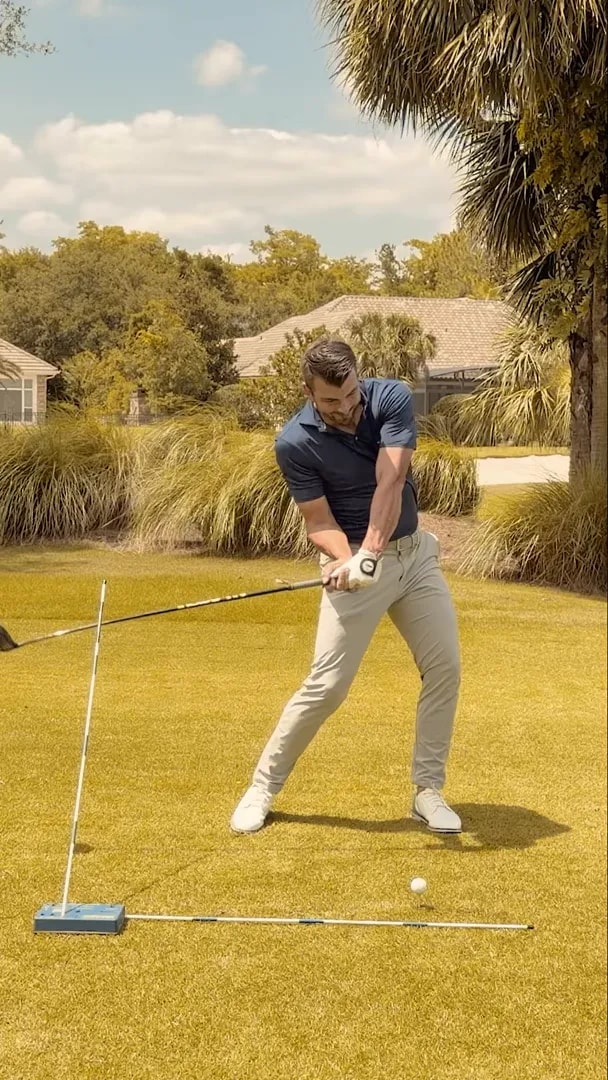 Face-on impact area with the training stick on the ground and the golfer's trail elbow tucked near the body