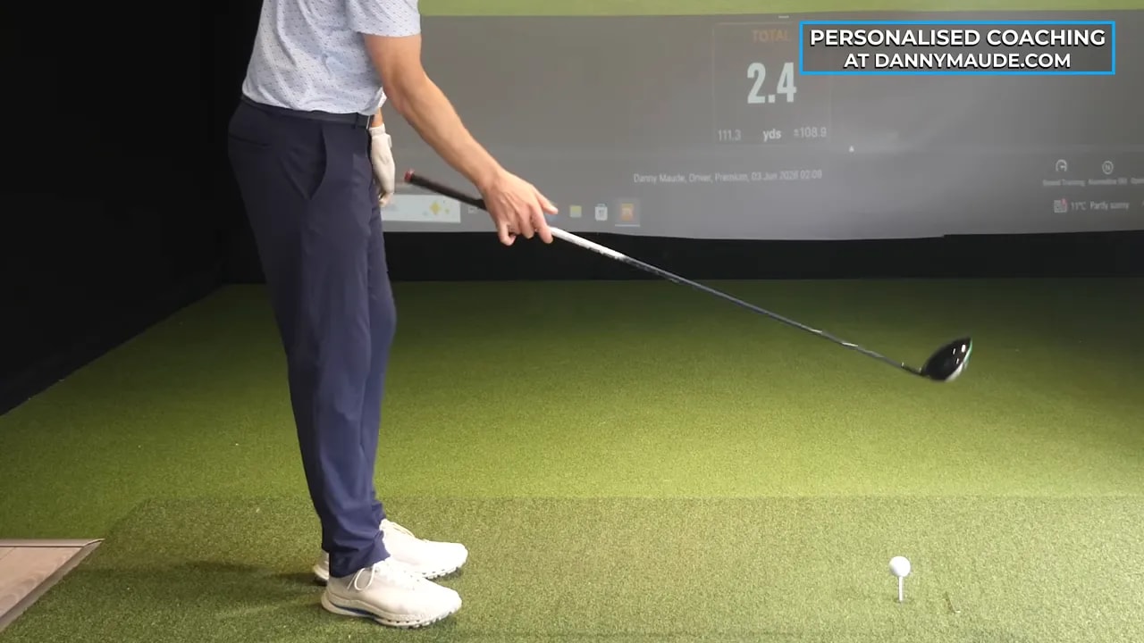 close view of one handed driver swing drill with clubhead moving past a tee