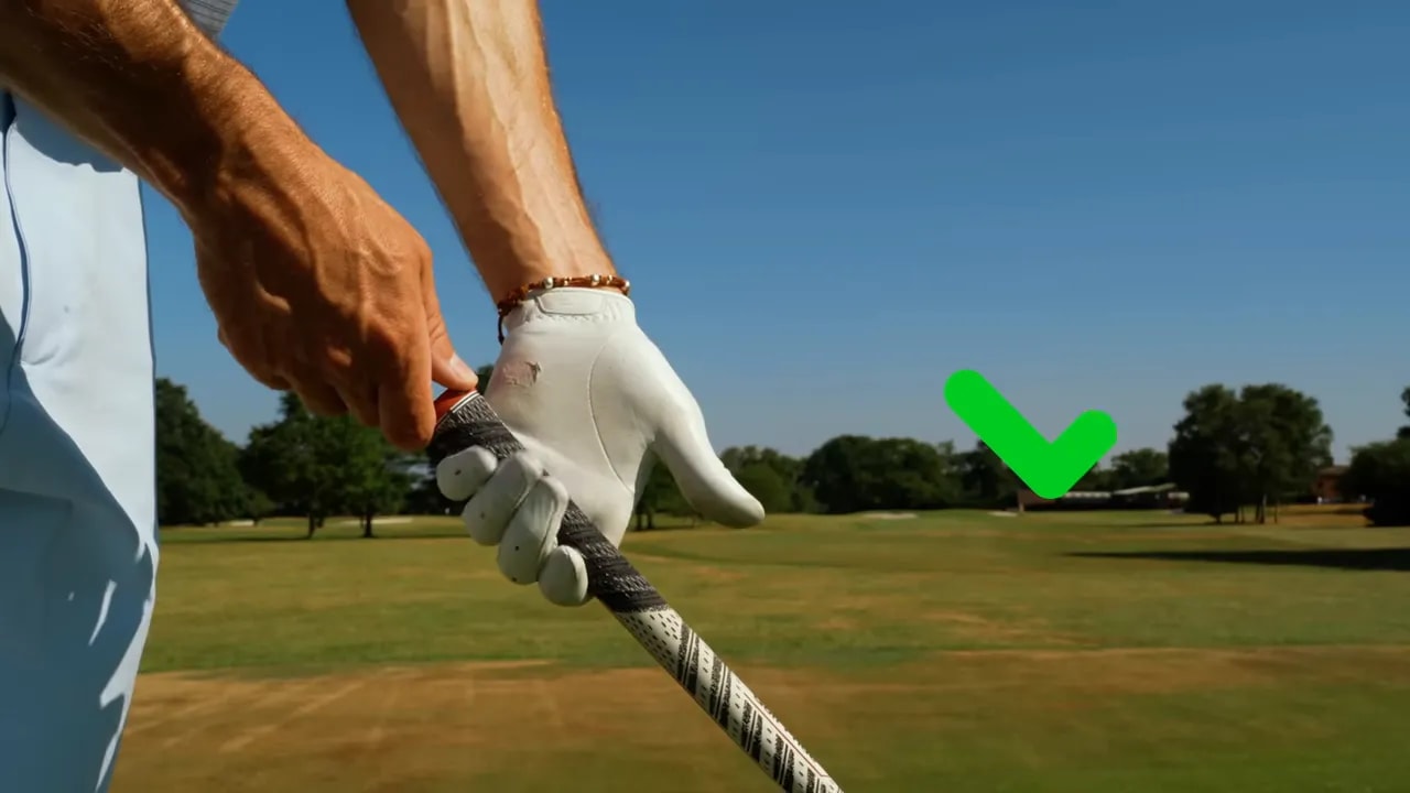 Close view of a gloved hand holding the club through the fingers with a green check mark