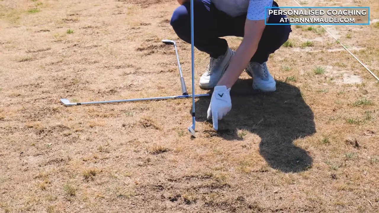 Close view of a golfer pointing to a divot marked ahead of the ball position line