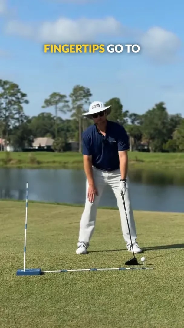 golfer bent at address with hand lowered toward right knee and driver behind ball