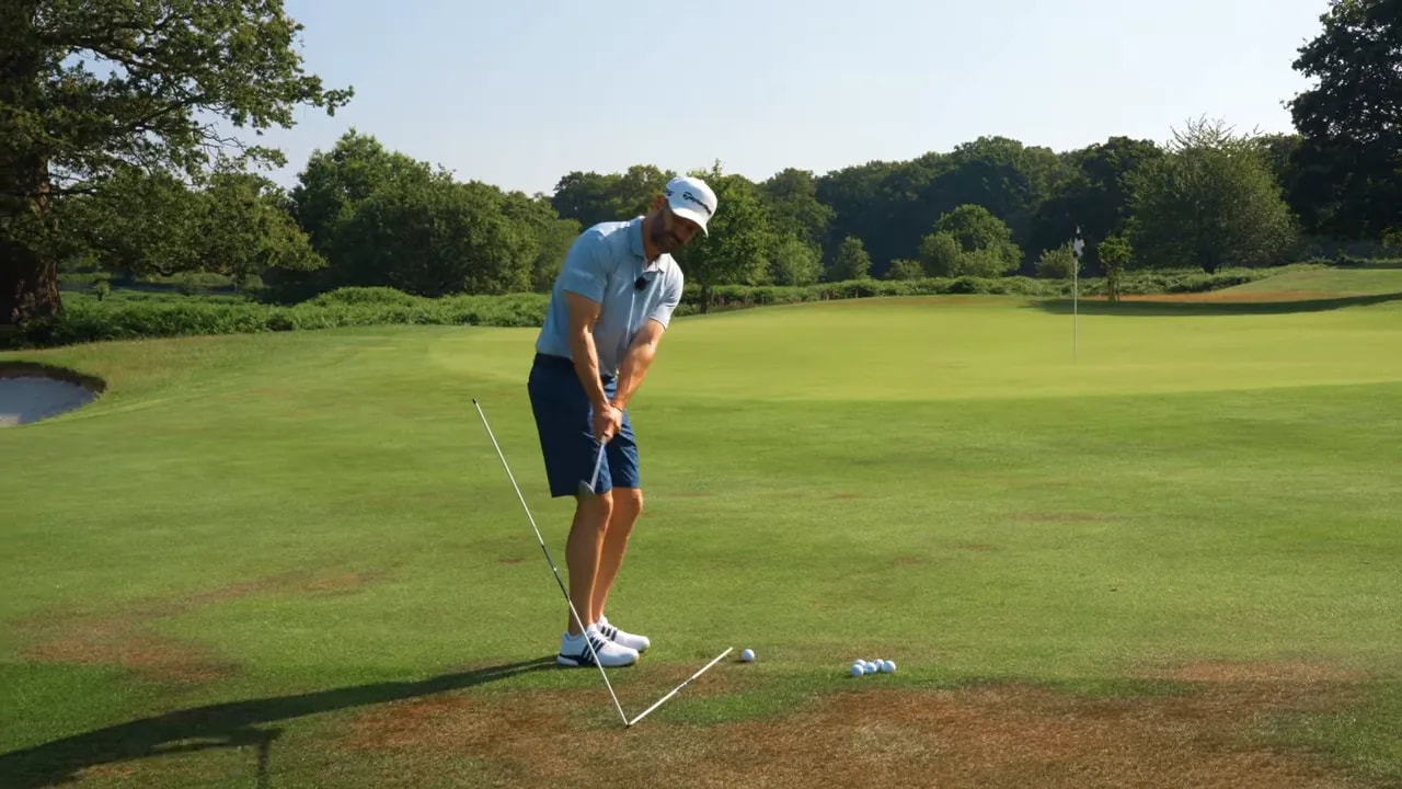 Golf practice station with two alignment sticks beside a wedge and balls