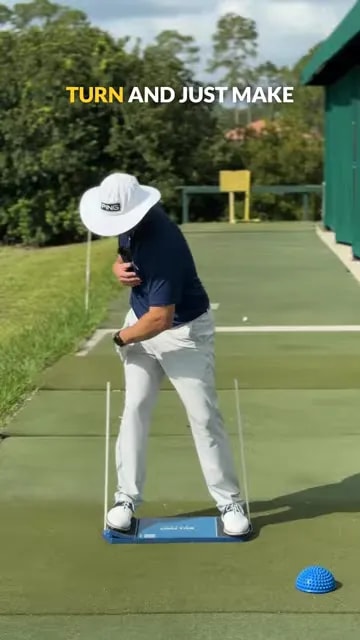 golfer turning in backswing on blue board with rear alignment stick beside the trail hip