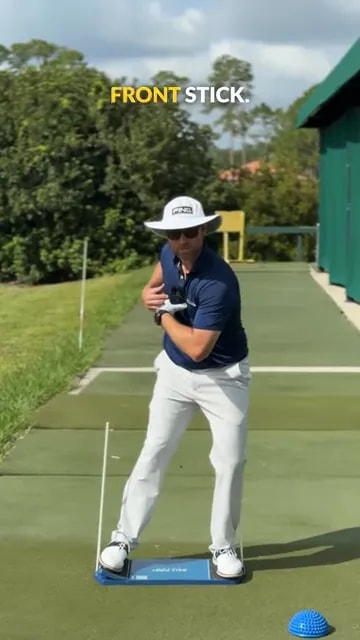 golfer paused in transition with two alignment sticks and a training board underfoot