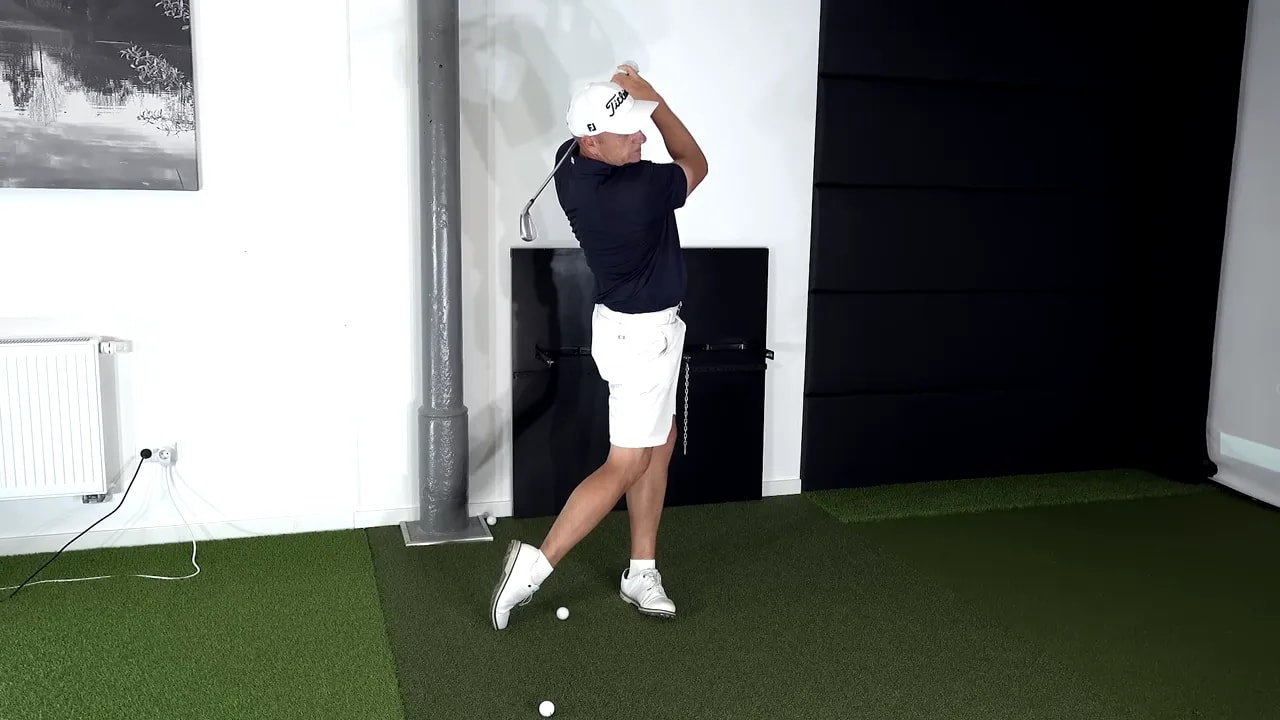instructor holding high finish with club across above head and lead side fully extended