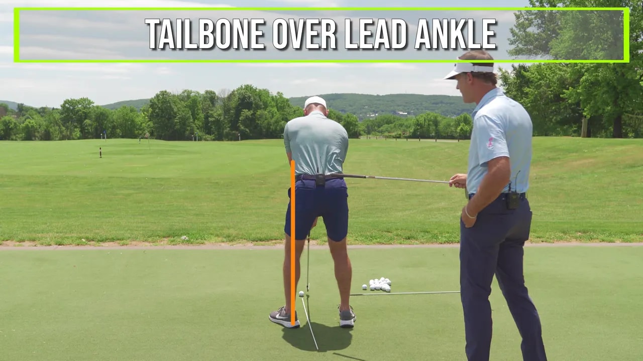 Rear view of golfer at top of backswing with orange line and text showing tailbone over lead ankle
