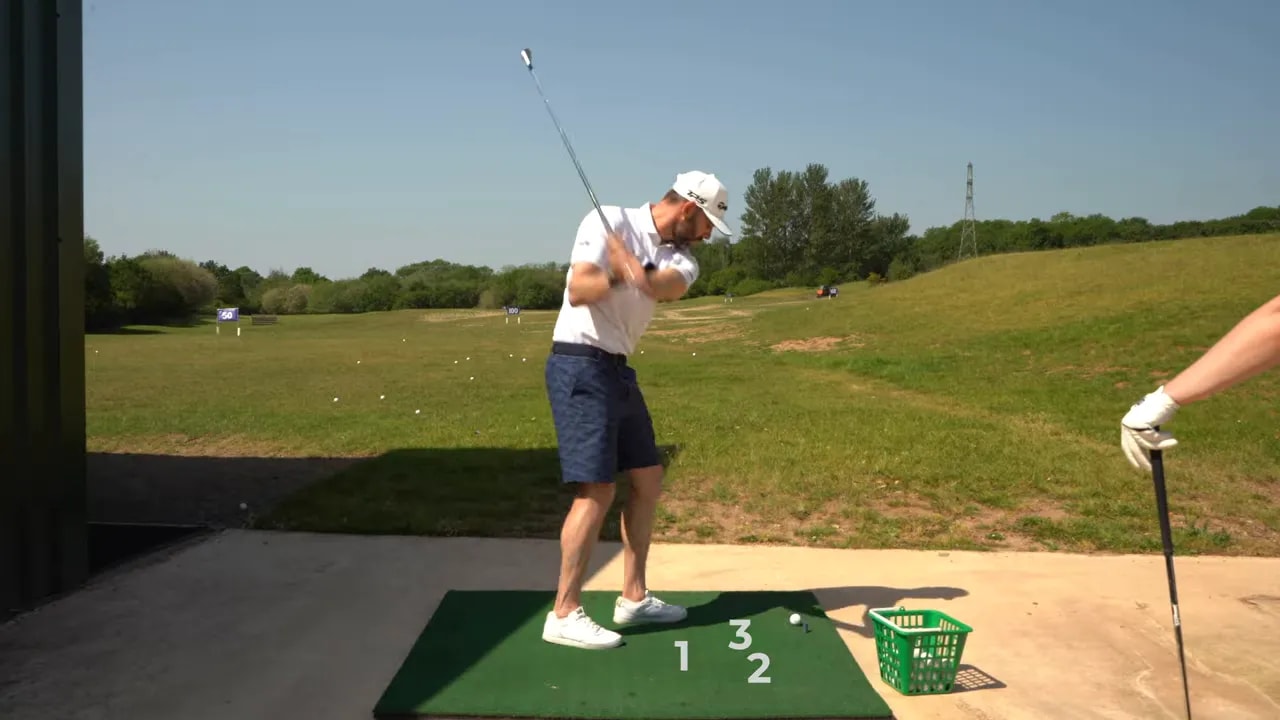 Coach making a short swing and striking down into the mat near several golf balls