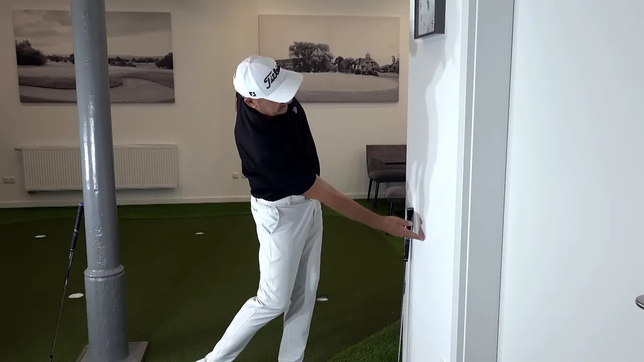golfer leaning toward wall with one hand touching the wall in a side bend position