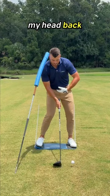 Golfer demonstrating head position behind the ball with a blue foam alignment guide