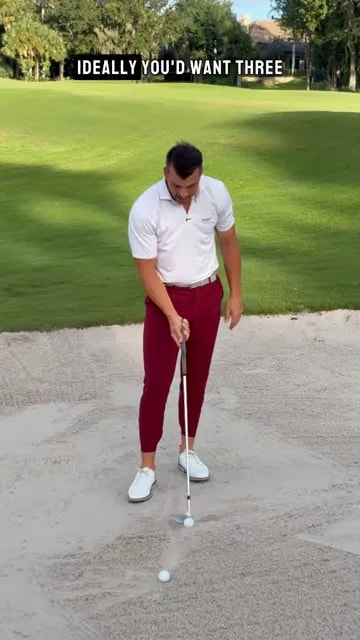 Golfer pointing at a spot in the sand several inches behind a golf ball