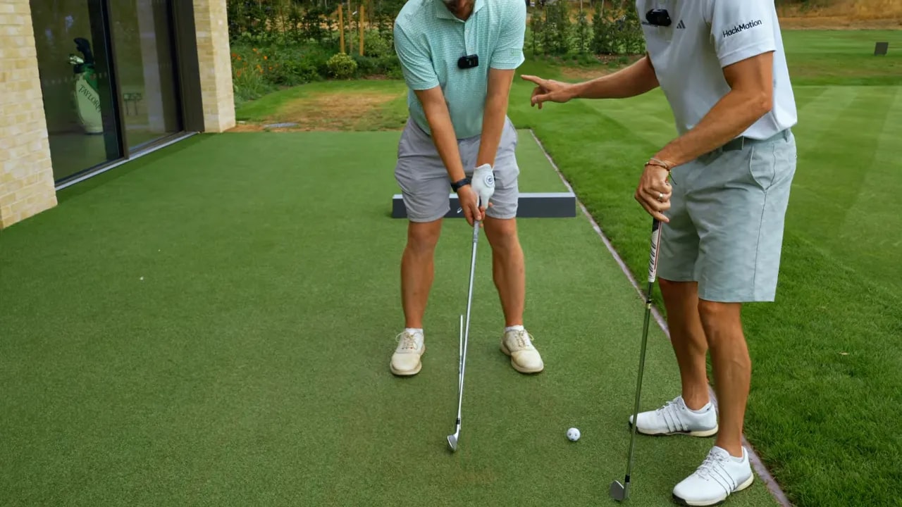 Coach placing a golf ball far forward beside an alignment stick on the practice mat